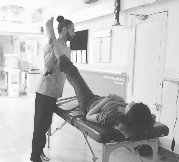 Therapist assisting a woman lying on a treatment table with leg stretch in a bright room.